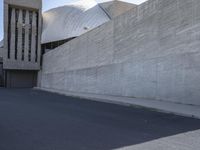 the view down a parking lot towards an abstract building with white stucco and light concrete walls