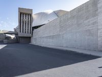 the view down a parking lot towards an abstract building with white stucco and light concrete walls