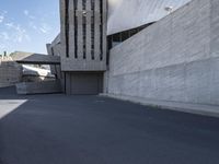 the view down a parking lot towards an abstract building with white stucco and light concrete walls