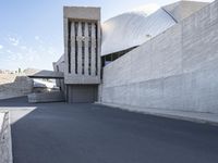 the view down a parking lot towards an abstract building with white stucco and light concrete walls