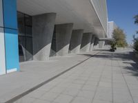 a walkway that leads to a building with columns on each side of it that has trees and plants on the ground