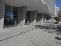 a walkway that leads to a building with columns on each side of it that has trees and plants on the ground
