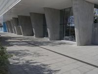 a walkway that leads to a building with columns on each side of it that has trees and plants on the ground