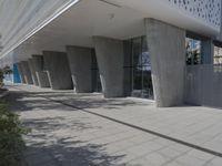 a walkway that leads to a building with columns on each side of it that has trees and plants on the ground