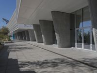 a walkway that leads to a building with columns on each side of it that has trees and plants on the ground