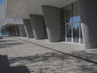 a walkway that leads to a building with columns on each side of it that has trees and plants on the ground