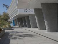 a walkway that leads to a building with columns on each side of it that has trees and plants on the ground
