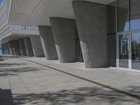 a walkway that leads to a building with columns on each side of it that has trees and plants on the ground
