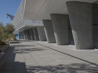 a walkway that leads to a building with columns on each side of it that has trees and plants on the ground