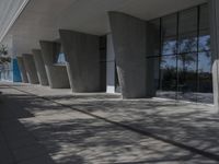 a walkway that leads to a building with columns on each side of it that has trees and plants on the ground