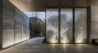 a glass and metal building with doors and lights at night with a view into the courtyard