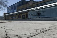 a small airplane sits on the pavement near an empty building with lots of windows at the base