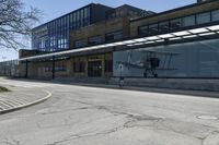 a small airplane sits on the pavement near an empty building with lots of windows at the base