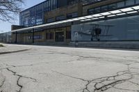 a small airplane sits on the pavement near an empty building with lots of windows at the base