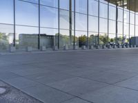 an empty pavement outside an office building with some glass windows on both sides and metal bins in the foreground