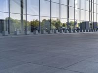 an empty pavement outside an office building with some glass windows on both sides and metal bins in the foreground