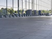 an empty pavement outside an office building with some glass windows on both sides and metal bins in the foreground