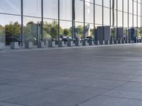 an empty pavement outside an office building with some glass windows on both sides and metal bins in the foreground