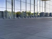 an empty pavement outside an office building with some glass windows on both sides and metal bins in the foreground