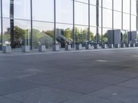 an empty pavement outside an office building with some glass windows on both sides and metal bins in the foreground