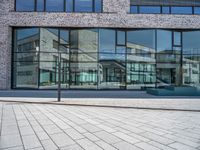 a sidewalk with no people in front of a large glass wall of a building, which is also on one side