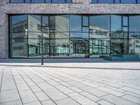 a sidewalk with no people in front of a large glass wall of a building, which is also on one side