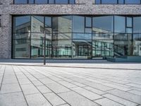 a sidewalk with no people in front of a large glass wall of a building, which is also on one side