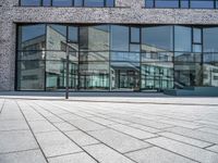 a sidewalk with no people in front of a large glass wall of a building, which is also on one side