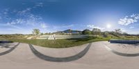 people riding skateboards on top of cement pavement at park with grassy field and house behind