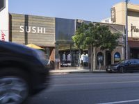 a car going past a building with a sushi sign on the front and behind it