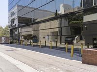 a sidewalk with benches on it and a building reflecting in the glass back wall and windows