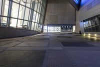 a walkway in an empty building with blue lighting on the doors and windows at night