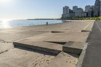 the concrete walkway has steps that go across it towards the water and to the city skyline