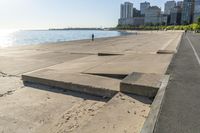 the concrete walkway has steps that go across it towards the water and to the city skyline