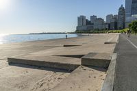 the concrete walkway has steps that go across it towards the water and to the city skyline