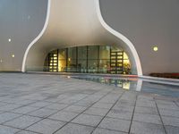 a photo of an exterior building with windows and lights reflecting in a puddle on the floor