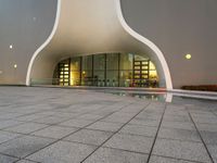 a photo of an exterior building with windows and lights reflecting in a puddle on the floor