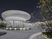 white building with circular lights in front and trees around it, lit by night sky