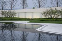 an empty pool and some trees and plants in the background with water reflecting the windows