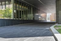 the view of an overpass under a building with grass and a bench in it