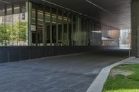 the view of an overpass under a building with grass and a bench in it