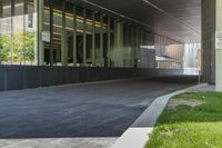 the view of an overpass under a building with grass and a bench in it