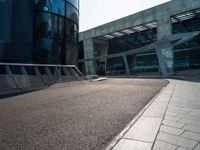 a skateboarder is going around on a sidewalk near a big building's glass windows