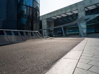 a skateboarder is going around on a sidewalk near a big building's glass windows