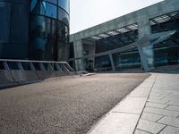 a skateboarder is going around on a sidewalk near a big building's glass windows