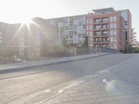 the sidewalk by the street is empty and sun shines on it and the city has very tall buildings in front