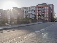 the sidewalk by the street is empty and sun shines on it and the city has very tall buildings in front