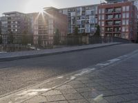 the sidewalk by the street is empty and sun shines on it and the city has very tall buildings in front