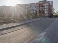 the sidewalk by the street is empty and sun shines on it and the city has very tall buildings in front
