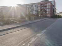 the sidewalk by the street is empty and sun shines on it and the city has very tall buildings in front